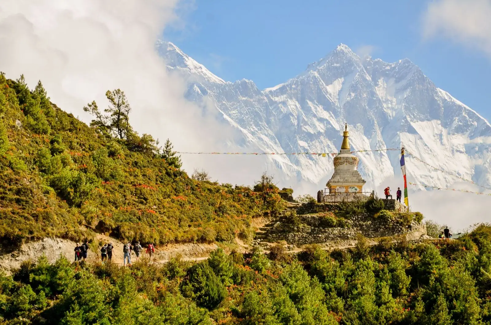 Excursionistas se acercan a una stupa con banderas de oración; al fondo, el Everest y el Lhotse.