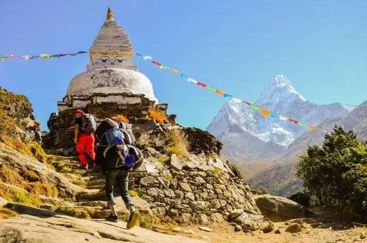 Un porteador y un excursionista pasan junto a una stupa con los ojos de Buda; a la derecha se alza el Ama Dablam.