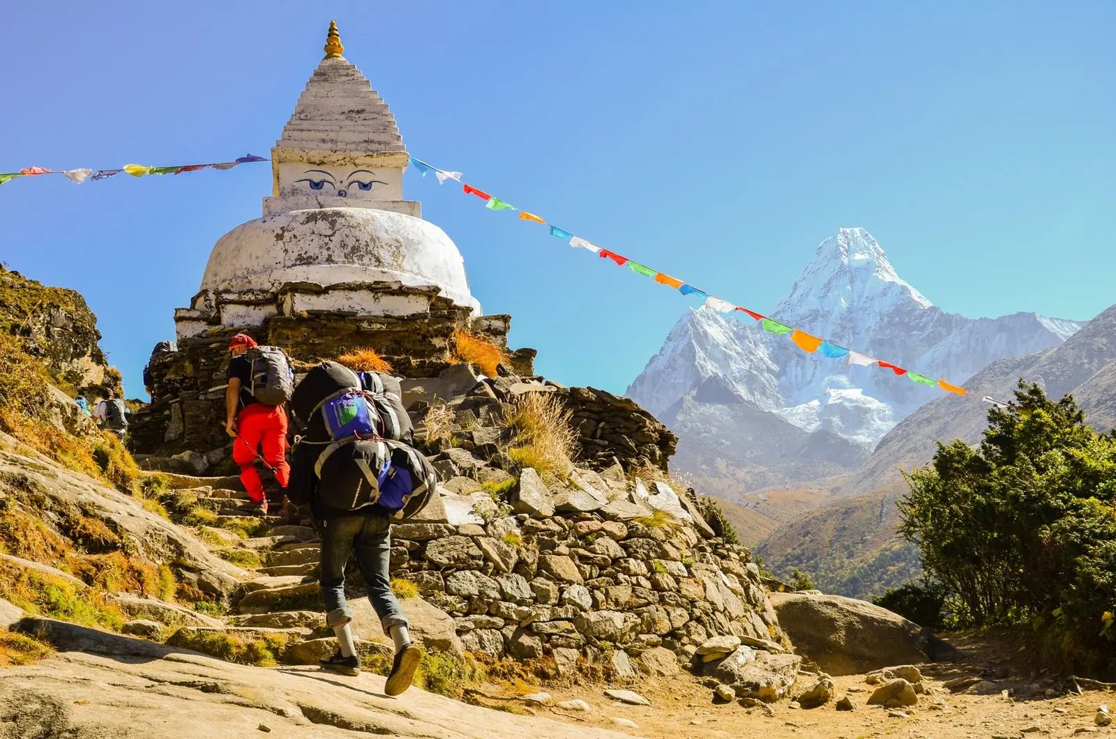 Un porteador y un excursionista pasan junto a una stupa con los ojos de Buda; a la derecha se alza el Ama Dablam.