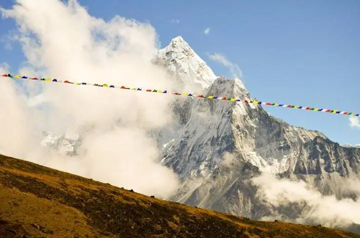 Banderas de oración ondean ante el Ama Dablam, envuelto en nubes.