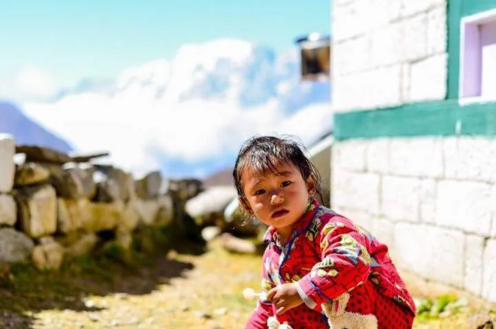 Un niño en una aldea del valle del Khumbu, junto a una casa de piedra encalada.